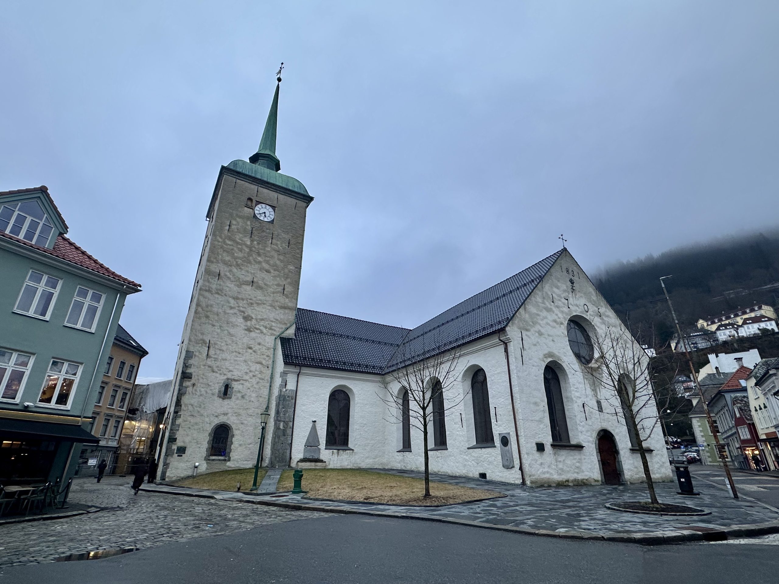 Vista exterior de la Catedral de Bergen, Domkirken, un edificio histórico de piedra blanca y torre con aguja verde en Noruega