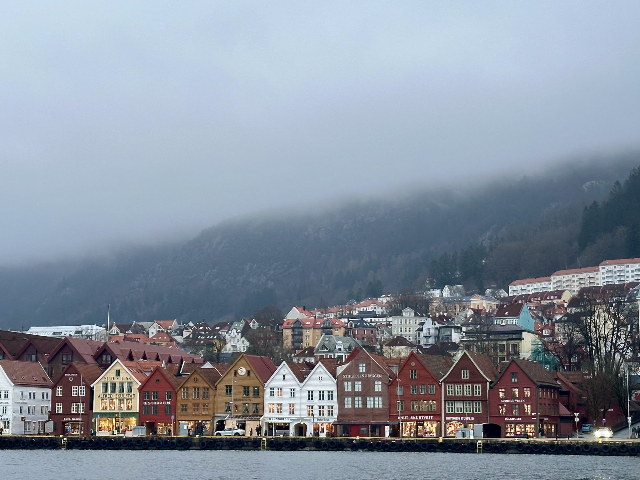 Panorámica del muelle de Bryggen en Bergen desde el agua, con sus casas de madera de colores y montañas cubiertas de niebla al fondo
