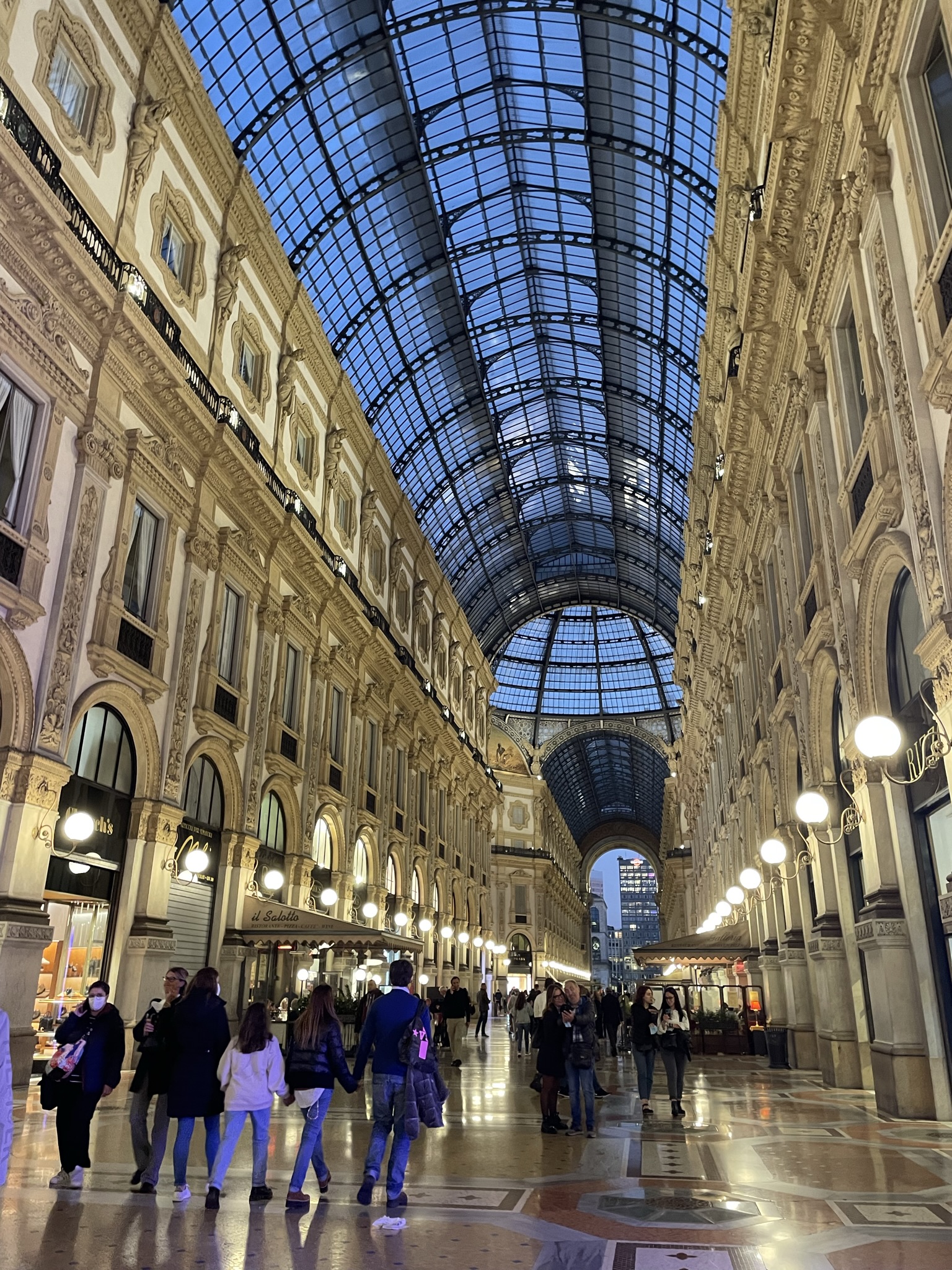 Interior de la Galleria Vittorio Emanuele II en Milán con techo acristalado, tiendas y ambiente elegante