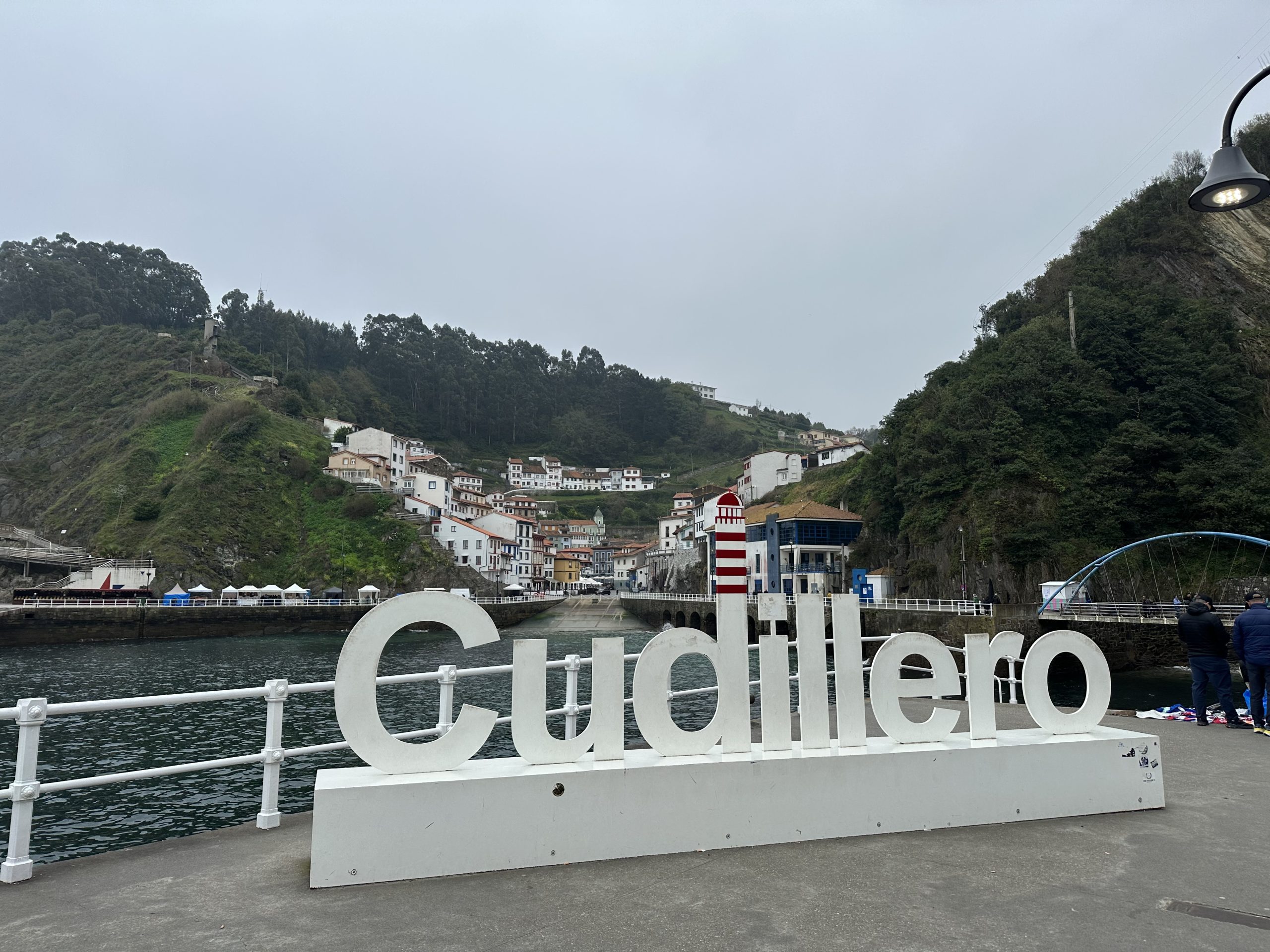 Letras de Cudillero junto al puerto con el pueblo marinero al fondo
