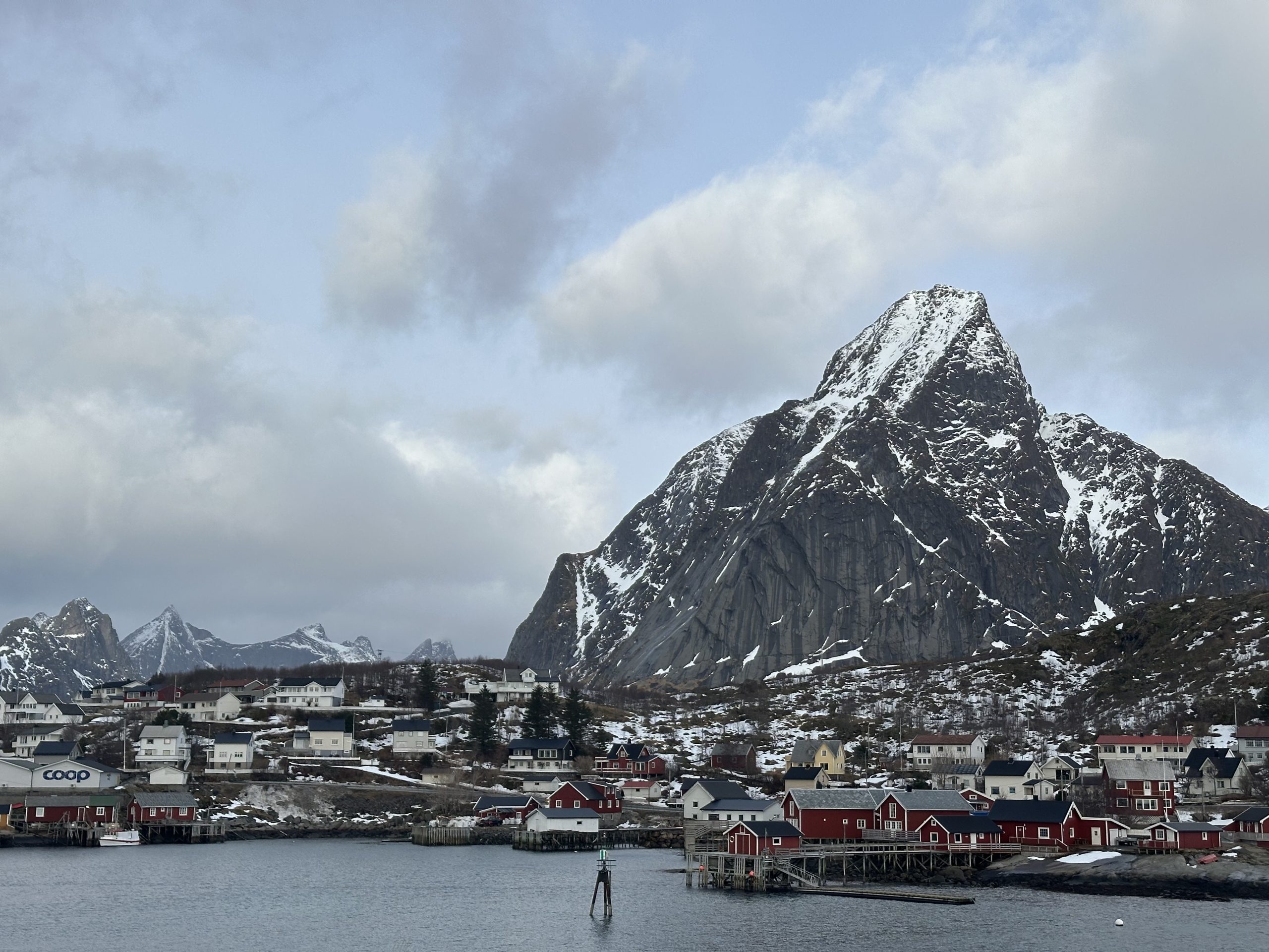 Paisaje de Reine con casas rojas, fiordo y montañas nevadas en Lofoten