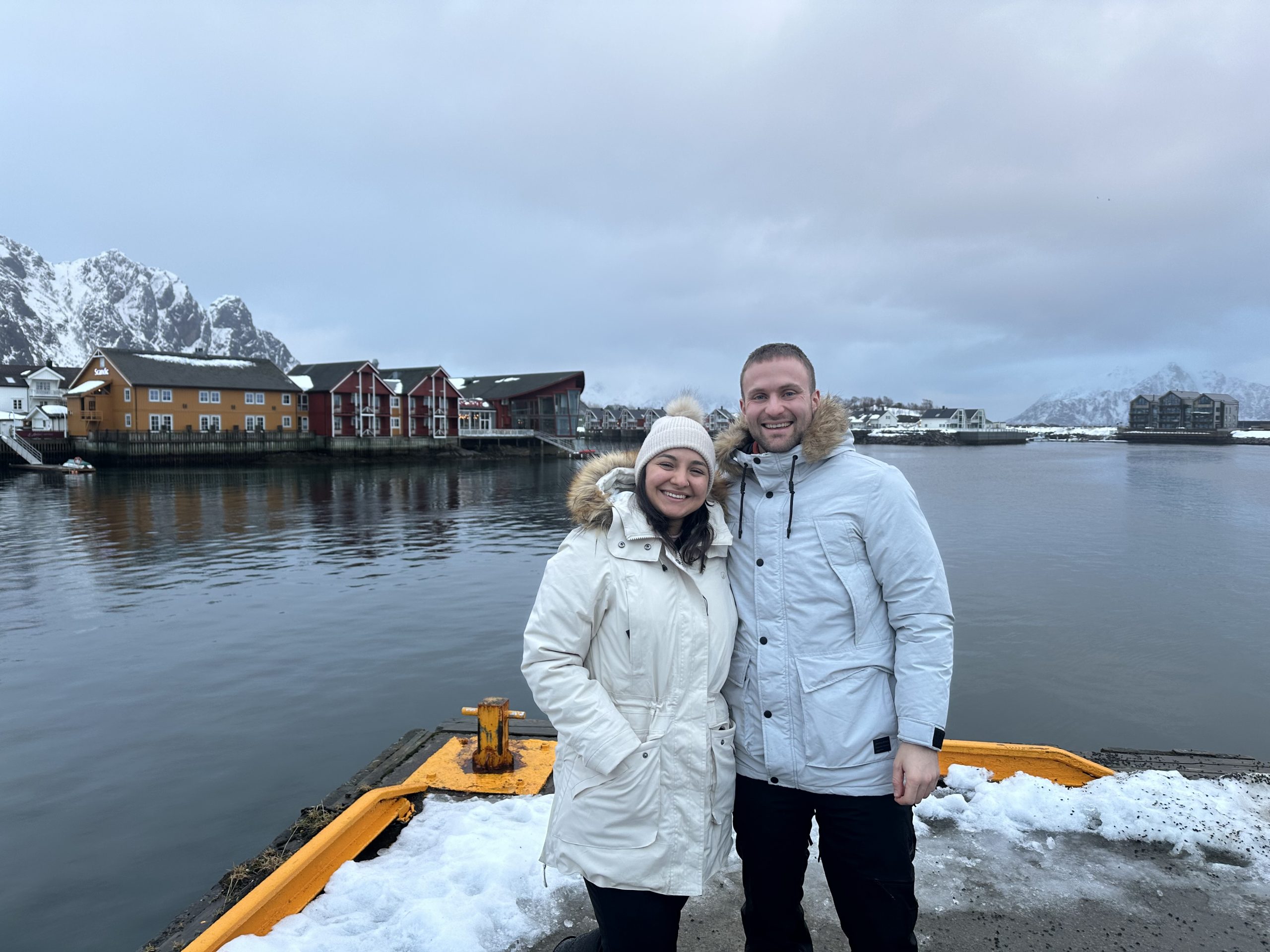 Pareja en el puerto de Svolvær con montañas nevadas al fondo