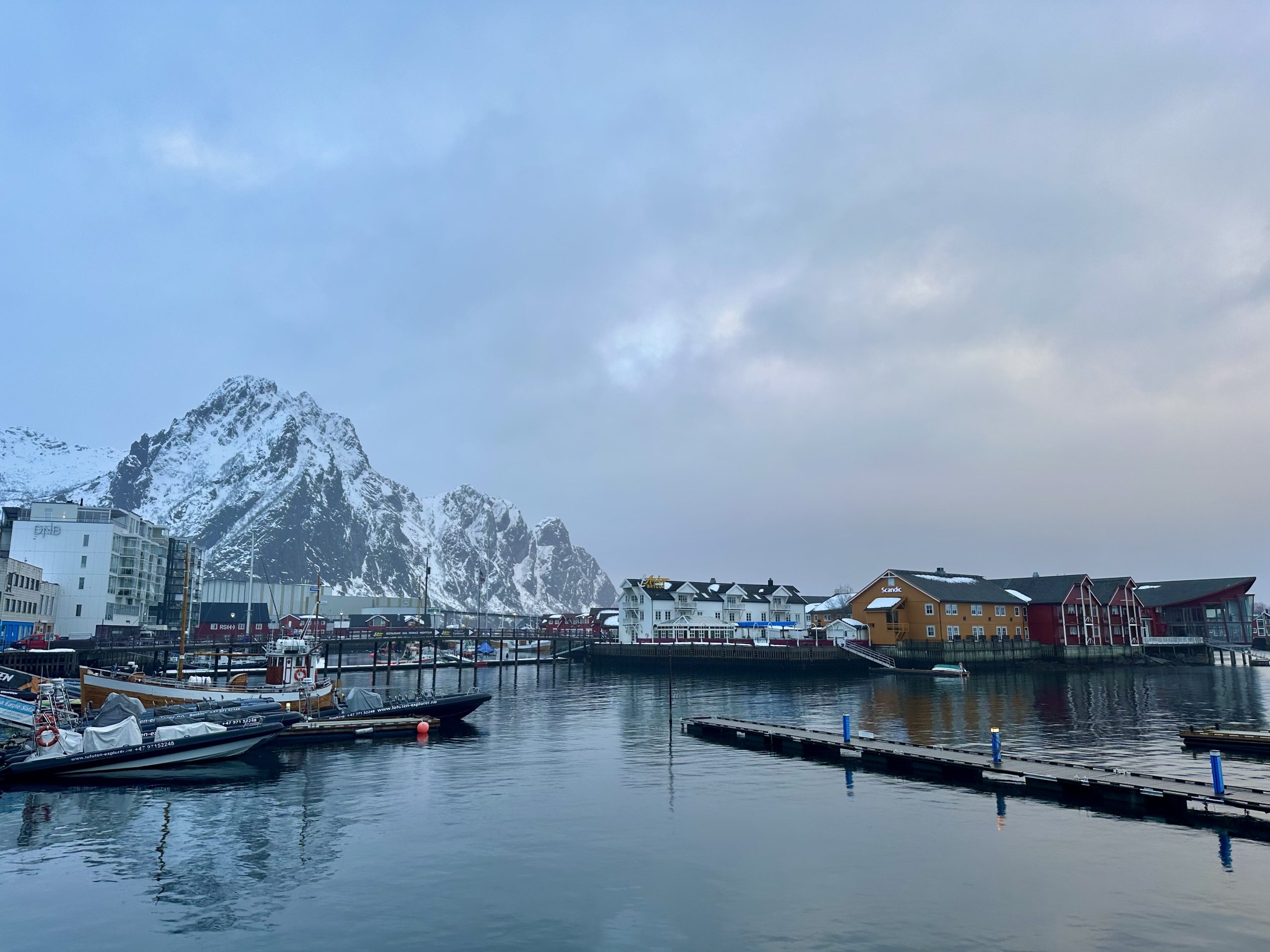 Puerto de Svolvær con casas tradicionales y montañas nevadas reflejadas en el agua