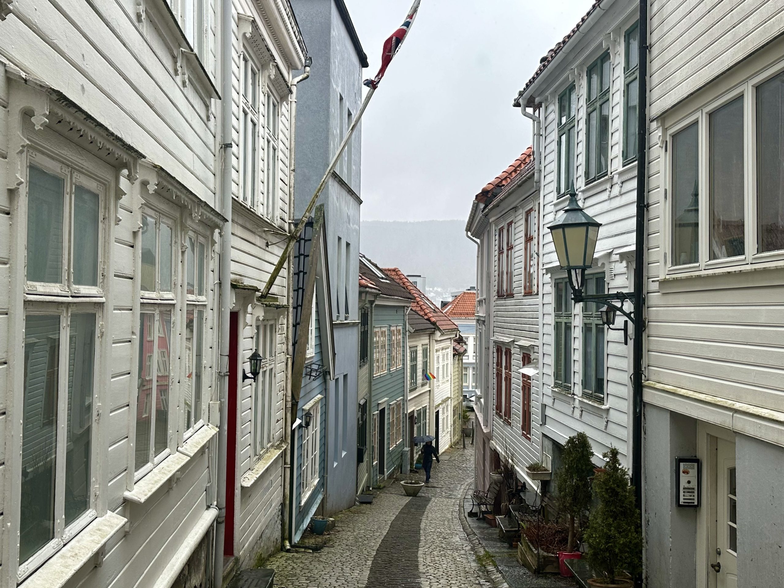 Callejón estrecho y empedrado con casas tradicionales de madera blanca y farolas en el centro histórico de Bergen, Noruega