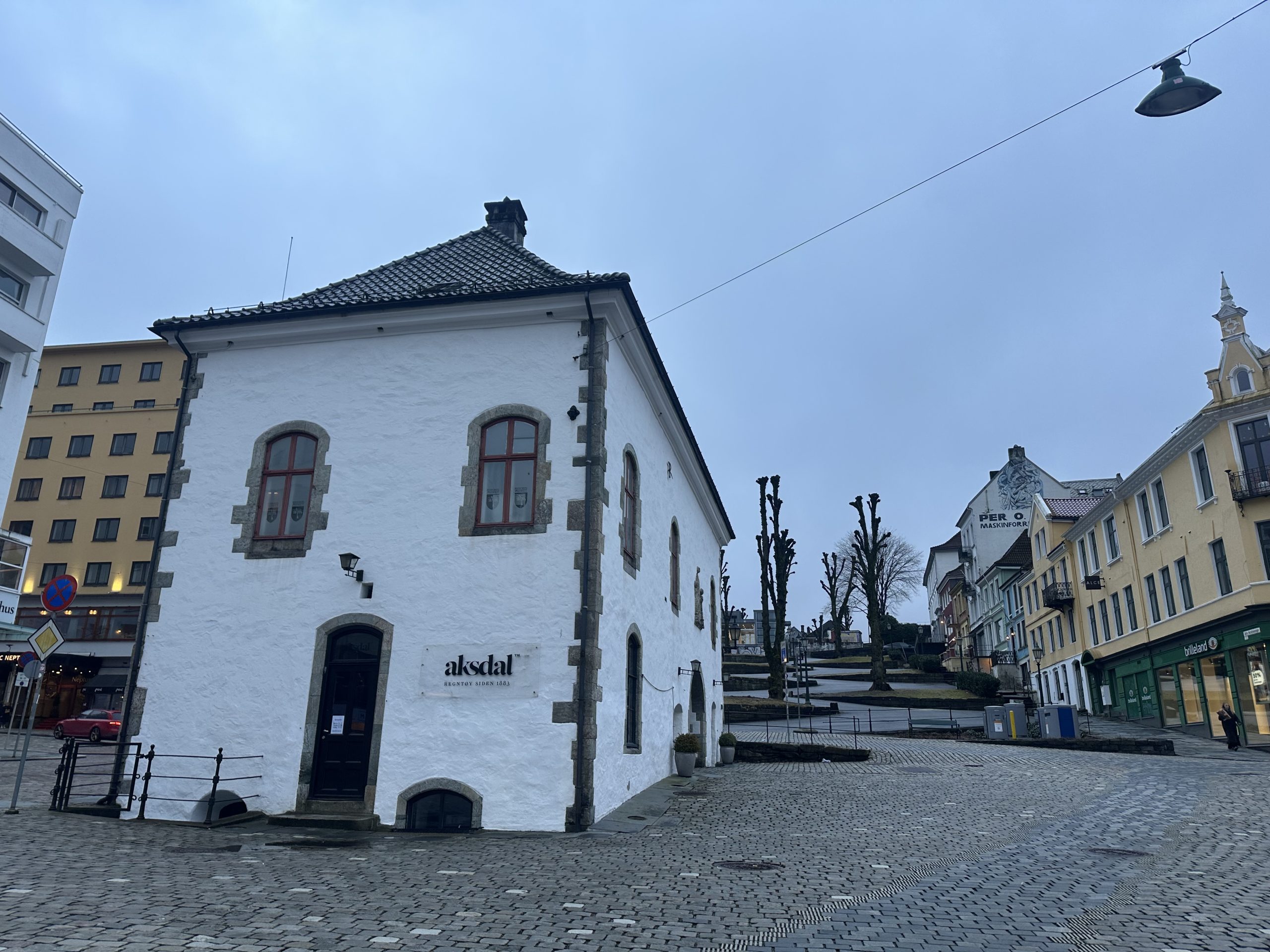 Edificio histórico blanco de la tienda Aksdal en una plaza empedrada del centro de Bergen, Noruega, en un día gris