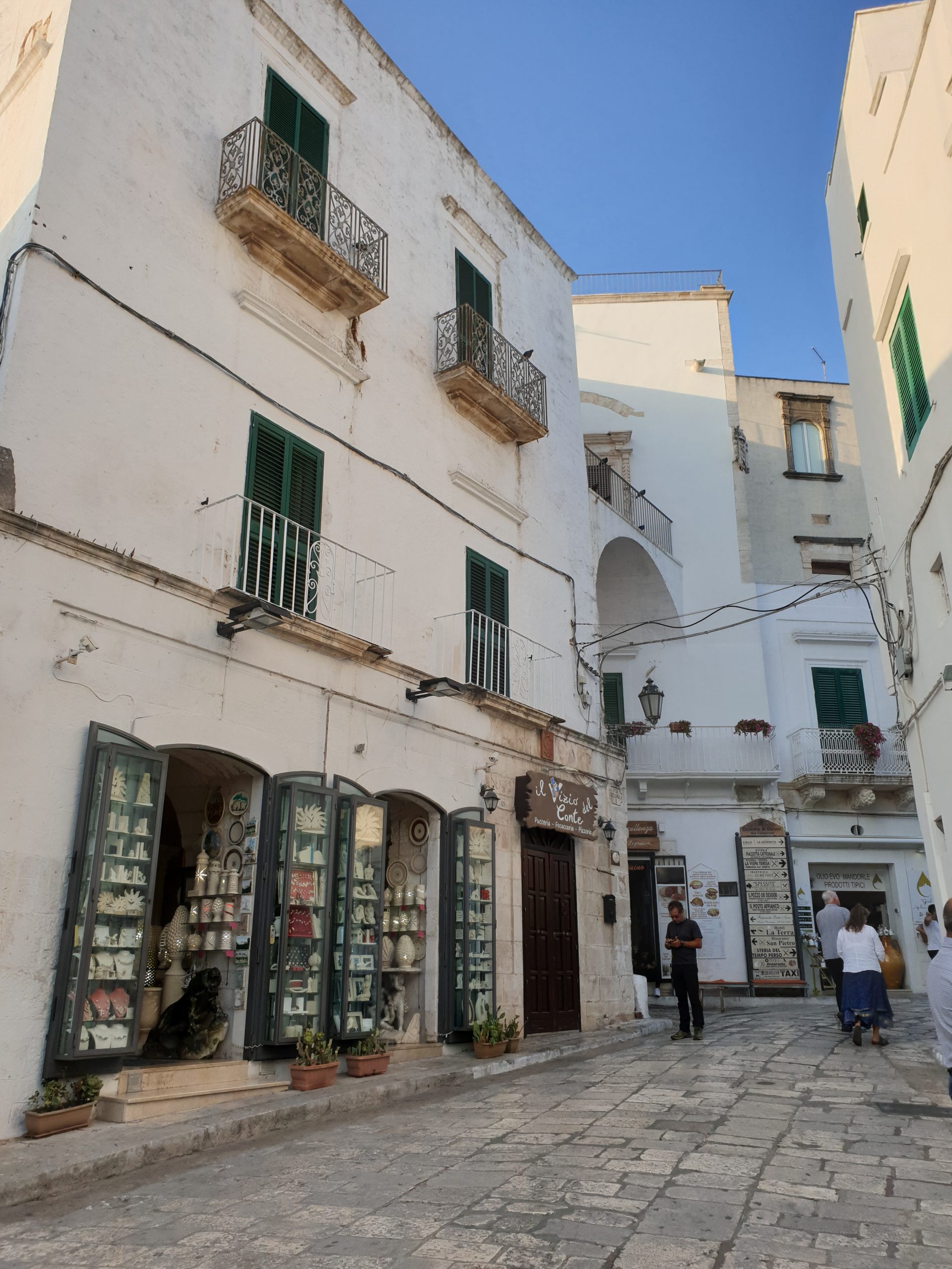 Callejuelas blancas de Ostuni con balcones, tiendas artesanales y suelo empedrado.