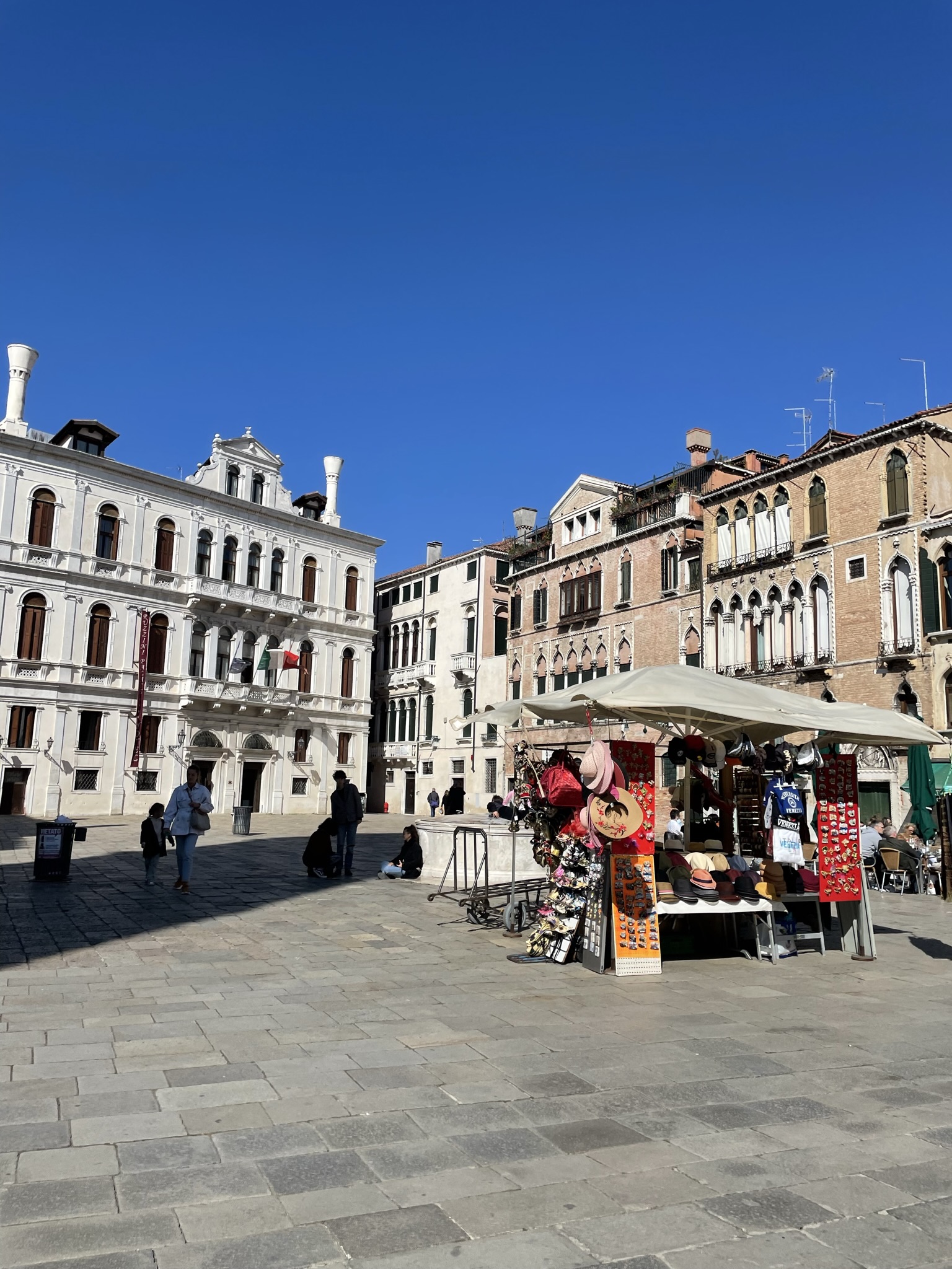 Campo Santo Stefano en Venecia, con edificios históricos, terrazas y puestos de recuerdos bajo el cielo azul.