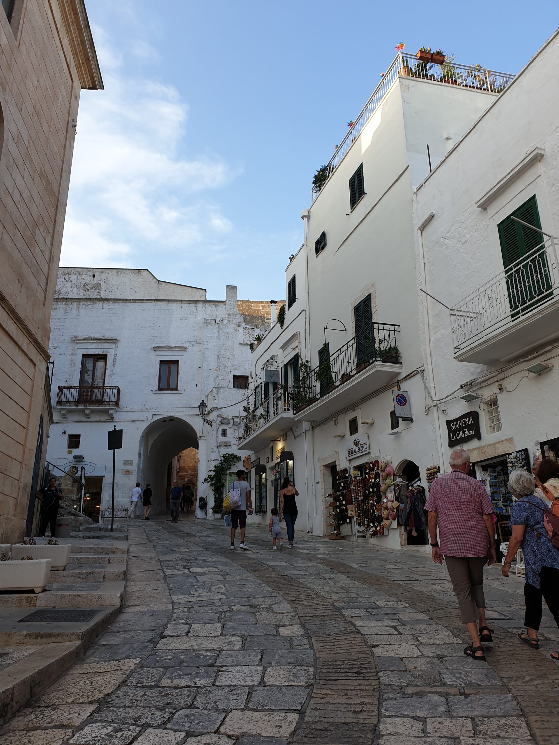 Calle empedrada del centro histórico de Ostuni con casas blancas, tiendas y ambiente local en la ciudad blanca de Apulia.