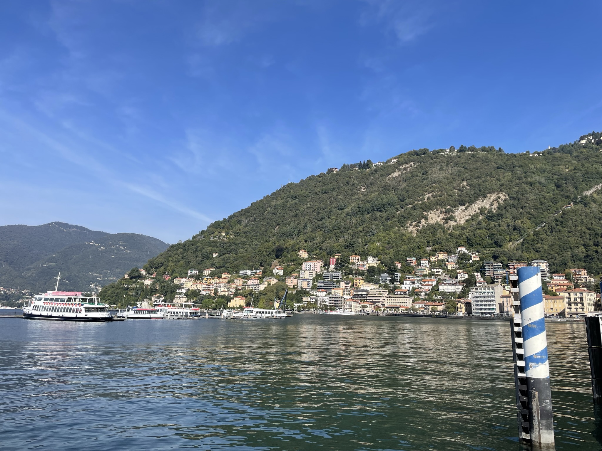 Paseo junto al Lago di Como con barcos, montañas y casas frente al agua