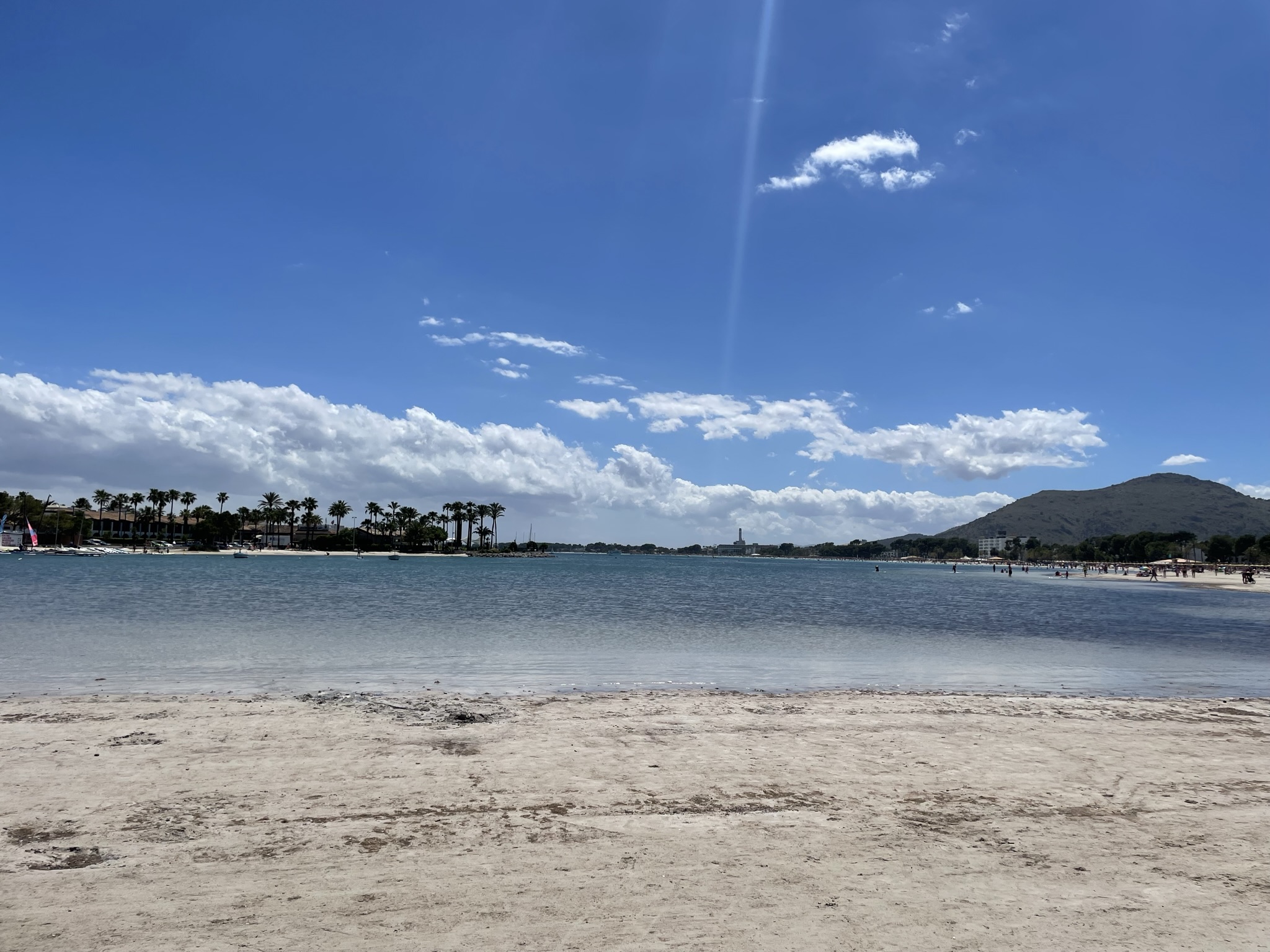 Playa de Alcudia en Mallorca con arena blanca, mar tranquilo y vistas al faro